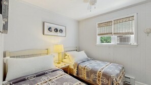 Ein Schlafzimmer mit zwei Betten, einem Nachttisch, einer Lampe und einem Fenster mit Jalousien.