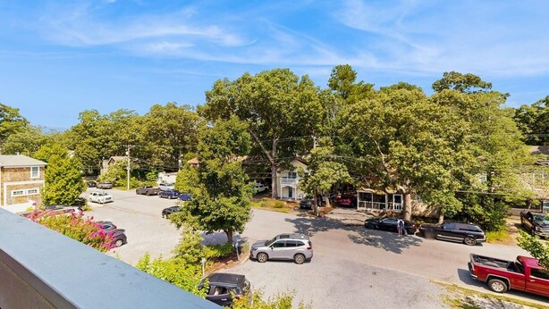 Un parking avec plusieurs voitures, des arbres et des bâtiments en arrière-plan.