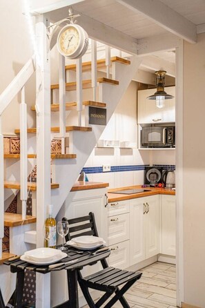 A kitchen with white cabinets, a wooden countertop, a microwave, and a hanging clock. - Kraków Podgórze Incognito Studio — Wawel & Old Town Nearby (Kraków)