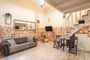 Uma sala de estar com sofá, televisão fixada na parede e escada que leva a outro andar.
