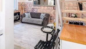 Une pièce avec un plafond en bois, un canapé, une table à manger avec des chaises et un coin cuisine avec une horloge.