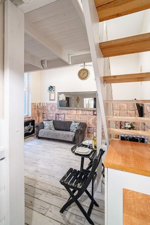 A room with a wooden ceiling, a sofa, a dining table with chairs, and a kitchen area with a clock. - Kraków Podgórze Incognito Studio — Wawel & Old Town Nearby (Kraków)