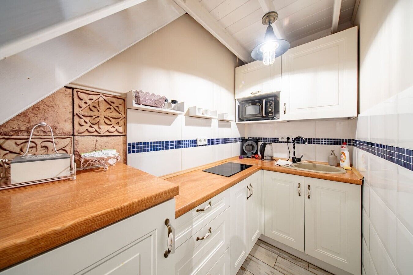 Een kleine keuken met witte kastjes, een houten aanrecht, een magnetron en een waterkoker.