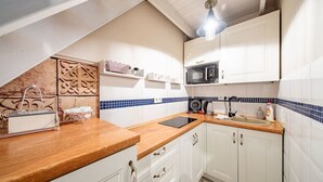 Une cuisine de taille réduite avec des meubles blancs, un plan de travail en bois, un four à micro-ondes et une bouilloire.
