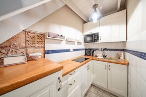 A compact kitchen with white cabinets, a wooden countertop, a microwave, and a kettle. - Kraków Podgórze Incognito Studio — Wawel & Old Town Nearby (Kraków)