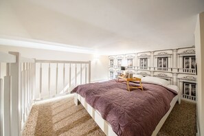 Um quarto com cama, mesa de cabeceira, janela e escada.