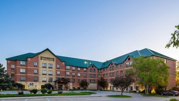 A Staybridge Inn with a brick facade, multiple floors, and a green roof. - Studio Suite w/ Jetted Tub | Free Breakfast! (West Des Moines)