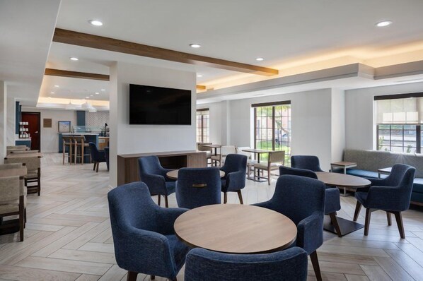 A modern hotel lobby with seating areas, a bar, and a television mounted on the wall.