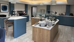 Ett modernt hotellrum med en stor köksö, en sittgrupp och en vägg med ett fiskbensmönster.