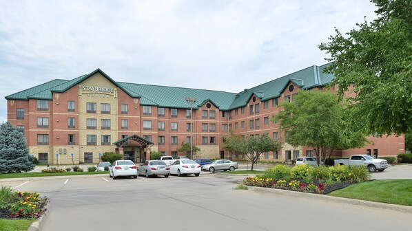 A Staybridge Suites hotel with a brick facade, green roof, and a parking lot with several cars.