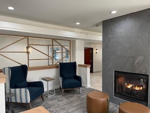 A modern lobby with two blue armchairs, a small side table, a fireplace, and a geometric wall design.