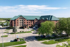 A large brick building with a green roof, a parking lot, and surrounding greenery. - Accessible Studio Suite w/ Tub | Free Breakfast! (West Des Moines)