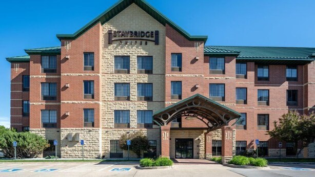A Staybridge hotel with a brick facade, multiple windows, and a covered entrance. - Accessible Studio Suite w/ Tub | Free Breakfast! (West Des Moines)