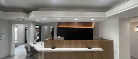 Un área de recepción con mostrador de madera, luces empotradas en el techo y diseño moderno.