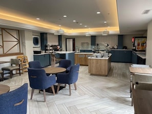 A modern hotel lobby with a central island, seating area, and a kitchenette.