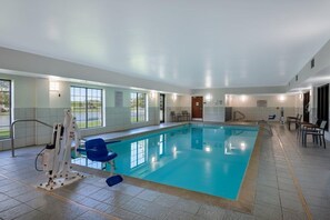 An indoor swimming pool with clear glass walls, a lifeguard stand, and a poolside seating area. - Accessible Studio w/ Roll-In Shwr | Free Breakfast (West Des Moines)