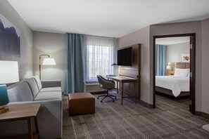 A hotel room with a bed, a desk, a chair, a sofa, a TV, and a window with curtains. - Accessible Studio w/ Roll-In Shwr | Free Breakfast (West Des Moines)