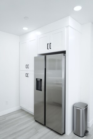Eine moderne Küche mit weißen Schränken, einem doppelwandigen Kühlschrank aus Edelstahl und einem Mülleimer.