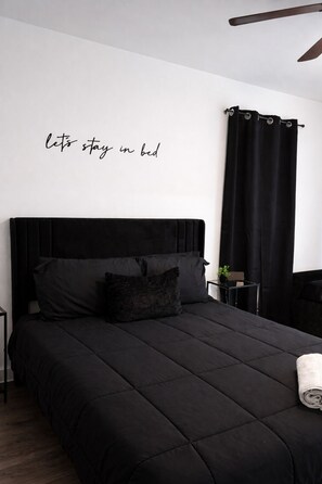 A modern bedroom with a black bed, a wall-mounted headboard, and a 'let's stay in bed' sign. - Tranquil 3-bedroom townhome with AC in Houston (Houston)