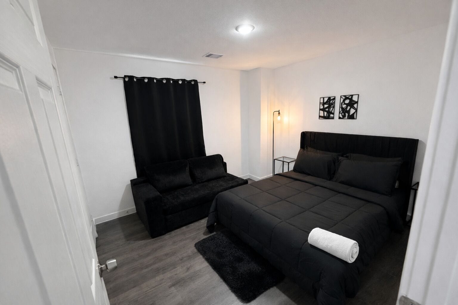 A bedroom with a bed, a sofa, a floor lamp, and artwork on the wall.