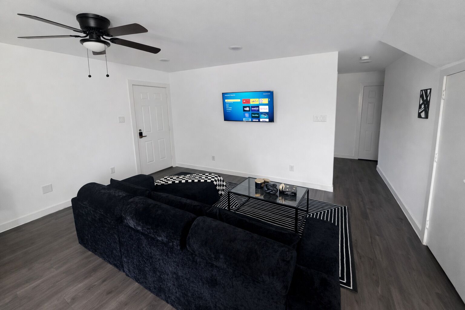 A modern living room with a black sofa, a glass coffee table, and a ceiling fan.