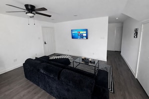 A modern living room with a black sofa, a glass coffee table, and a ceiling fan. - Tranquil 3-bedroom townhome with AC in Houston (Houston)