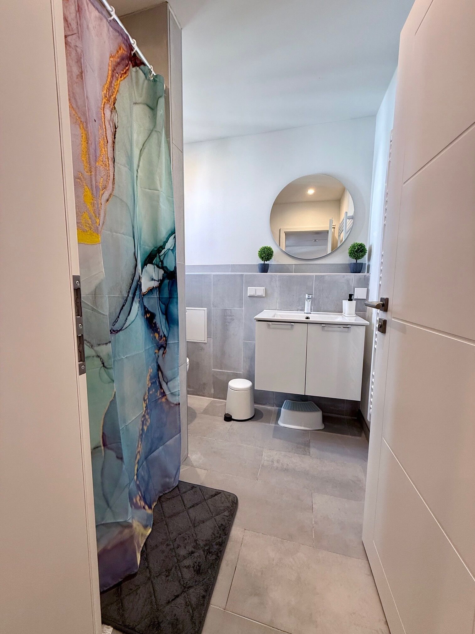 A modern bathroom with a shower curtain, a sink, a toilet, and a small step stool.