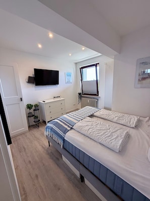 A bedroom with a bed, a dresser, a TV, and a window with curtains.