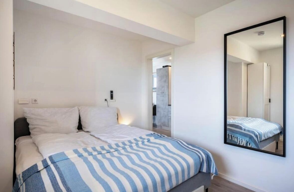 A modern bedroom with a bed, a large mirror, and a view of a bathroom.