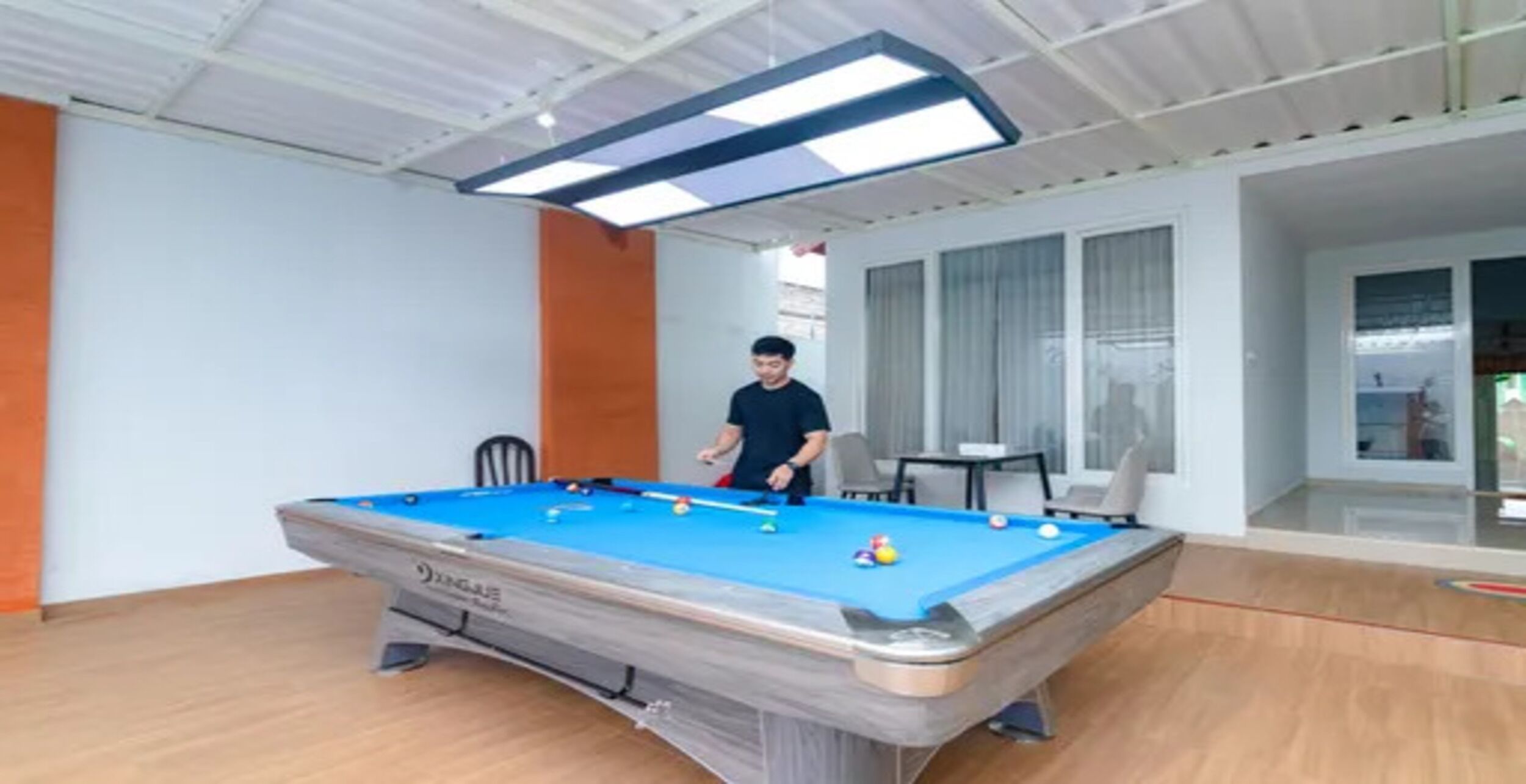 A pool table with a person playing, a chair, and a table with a laptop.