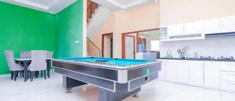 A pool table in a room with a green wall, a staircase, and a kitchen area.