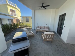 Eine Terrasse im Freien mit Grill, Sitzgelegenheit und Deckenventilator.