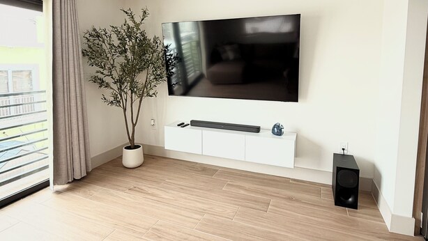 Una sala de estar moderna con un televisor de pantalla plana montado en la pared, una planta en maceta, un mueble blanco para entretenimiento y piso de madera.
