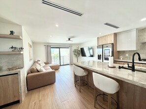A modern kitchen with a central island, bar stools, a built-in oven, and a large flat-screen TV. - New Construction in Outdoor Resorts Long Key! (Layton)