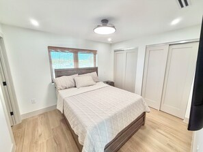 Ein Schlafzimmer mit einem Bett, einem Nachttisch, einem Fenster mit Jalousien und einem Deckenventilator.