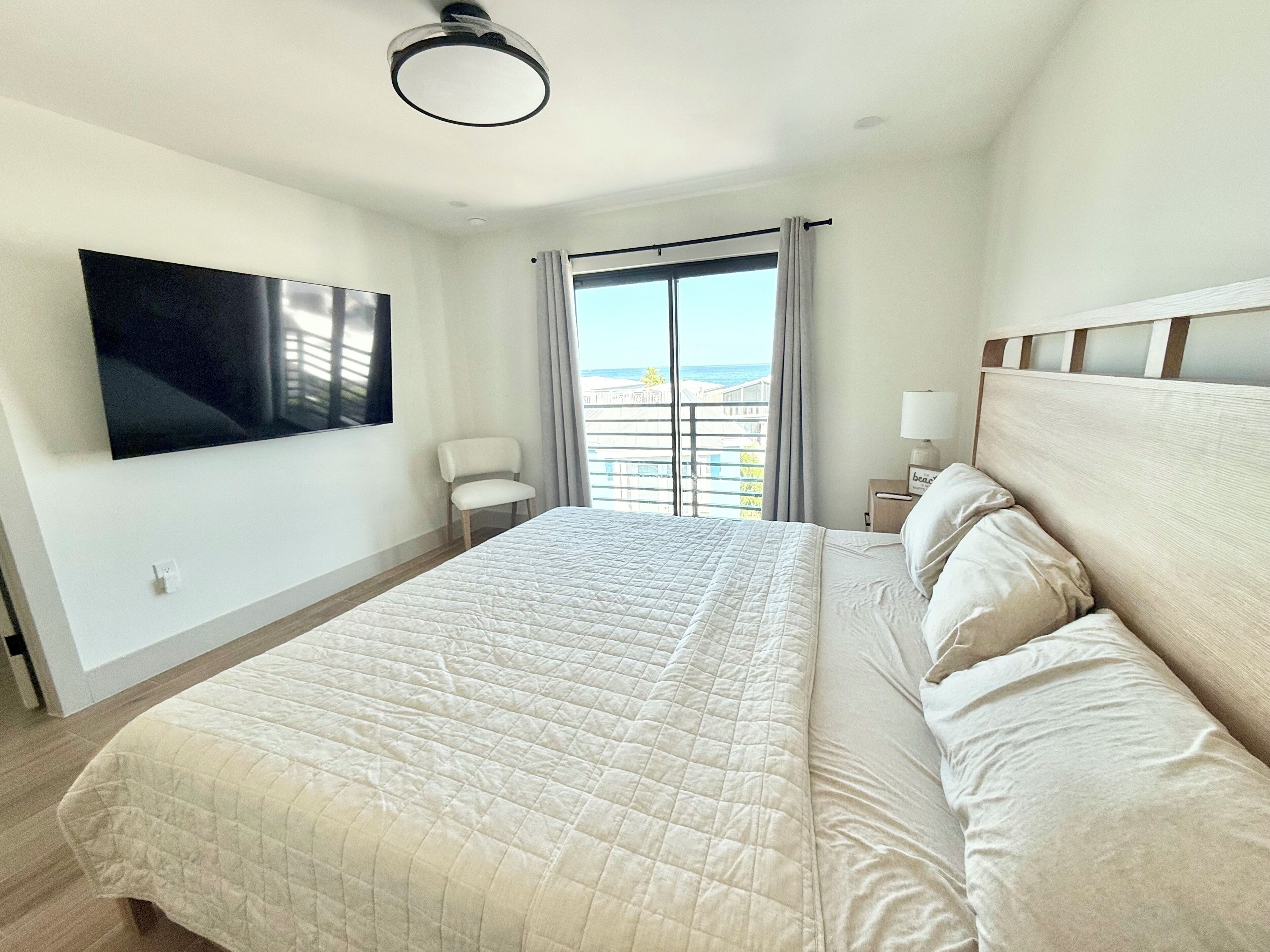 A hotel room with a bed, a chair, a TV, and a view of the sea.