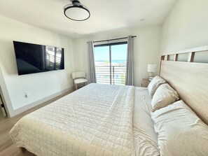 Een hotelkamer met een bed, een stoel, een televisie en uitzicht op zee.