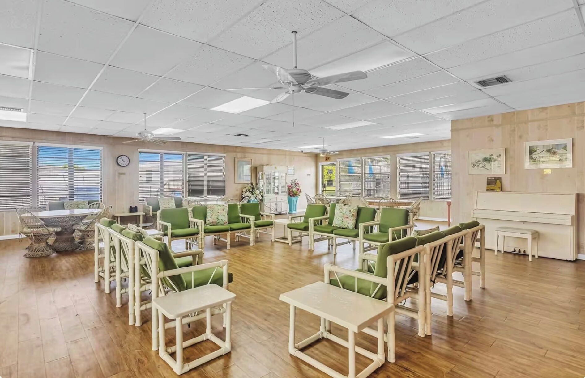 A spacious room with a ceiling fan, large windows with blinds, and a piano.