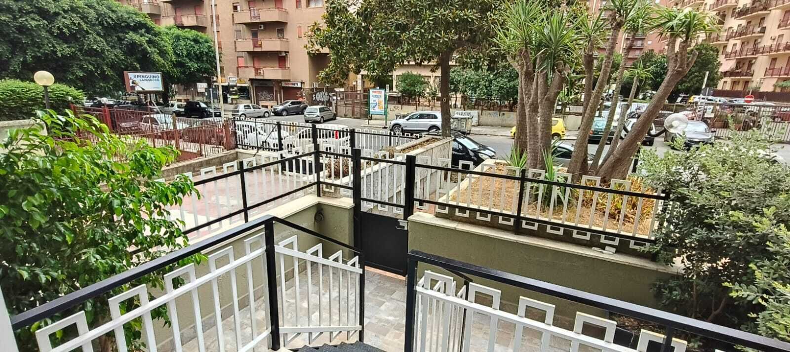 A multi-level outdoor area with a gated walkway, a water feature, and a view of a street with parked cars and buildings.