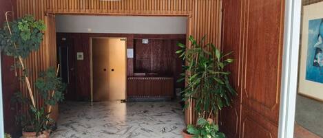 Un área de recepción con panel de madera, mostrador de recepción y plantas en macetas.