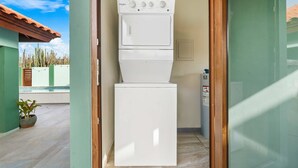 Una unidad compacta de lavadora y secadora Whirlpool blanca en un lavadero pequeño y cerrado, con vistas a una piscina y cactus al exterior.