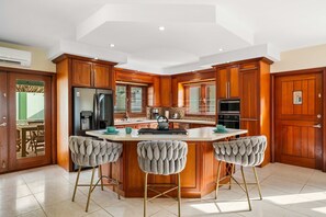 A kitchen with a central island, wooden cabinets, a refrigerator, and bar stools. - Alto Vista 107-h (Noord)