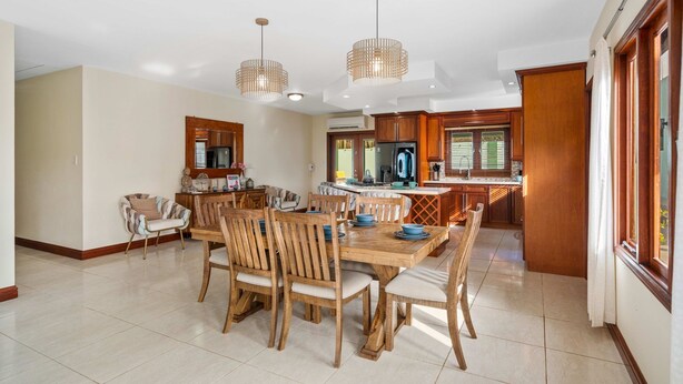 Un comedor amplio con una mesa y sillas de madera, una cocina al fondo y lámparas colgantes.