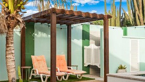 Un espacio de estar al aire libre cubierto con dos sillones de descanso, una pérgola de madera y una planta de cactus.