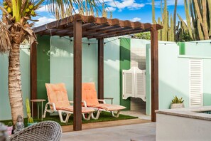 A covered outdoor seating area with two lounge chairs, a wooden pergola, and a cactus plant. - Alto Vista 107-h (Noord)