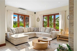A modern living room with a sectional sofa, a round coffee table, and large windows with curtains. - Alto Vista 107-h (Noord)
