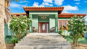 Una casa de dos plantas con fachada verde, una puerta de madera y un conjunto de escaleras que conducen a la entrada.