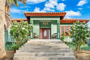 A two-story house with a green facade, a wooden door, and a set of stairs leading to the entrance. - Alto Vista 107-h (Noord)