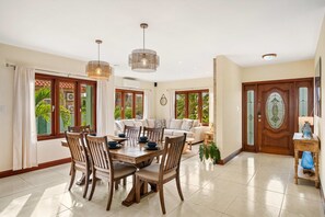 A dining area with a wooden table and chairs, a sofa, and a large window with a view of greenery. - Alto Vista 107-h (Noord)