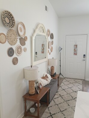 A room with a mirror, wall decor, a bench, a dog, a door, and a lamp. - Peaceful one bedroom Villa with Mediterranean decor (Palm Harbor)